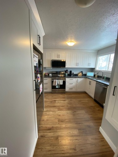 The kitchen features white cabinetry, dark countertops, and stainless steel appliances including a range, microwave, and refrigerator - 5030 40 Street, Cold Lake, AB - Indoor Photo Showing Kitchen