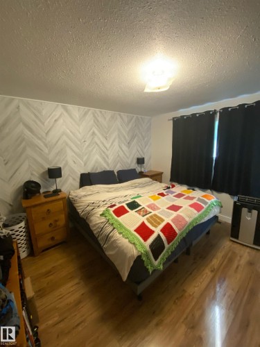 This room features a distinct accent wall with a herringbone pattern, wood-style flooring, and a ceiling light fixture - 5030 40 Street, Cold Lake, AB - Indoor Photo Showing Bedroom