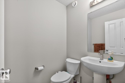 Pedestal sink with chrome faucet, wall-mounted mirror, overhead vanity lighting, and white toilet - 3214 9 Street, Edmonton, AB - Indoor Photo Showing Bathroom