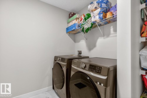 Dedicated laundry area featuring a front-load washer and dryer, light gray wall paint, white trim, and a wire shelving unit - 3214 9 Street, Edmonton, AB - Indoor Photo Showing Laundry Room