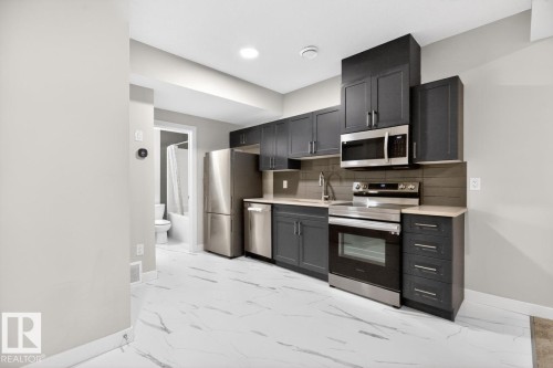 Kitchen featuring dark cabinetry, stainless steel appliances, light countertops, and a tiled backsplash - 3214 9 Street, Edmonton, AB - Indoor Photo Showing Kitchen With Stainless Steel Kitchen