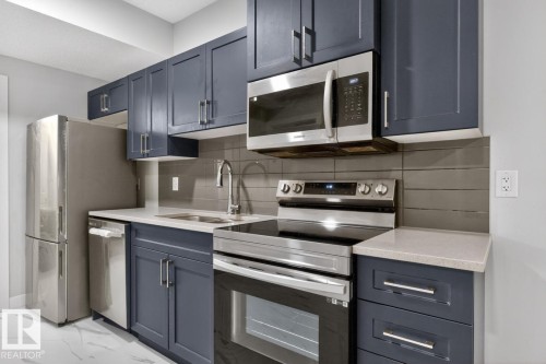 Kitchen featuring stainless steel appliances, blue shaker-style cabinetry, light-colored countertops, a tile backsplash, and a wall-mounted microwave - 3214 9 Street, Edmonton, AB - Indoor Photo Showing Kitchen With Stainless Steel Kitchen With Upgraded Kitchen