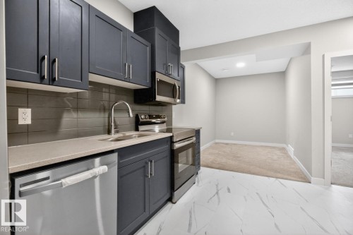 Contemporary kitchen featuring dark cabinetry, stainless steel appliances, a light-toned countertop, and a sleek tile backsplash - 3214 9 Street, Edmonton, AB - Indoor Photo Showing Kitchen With Double Sink