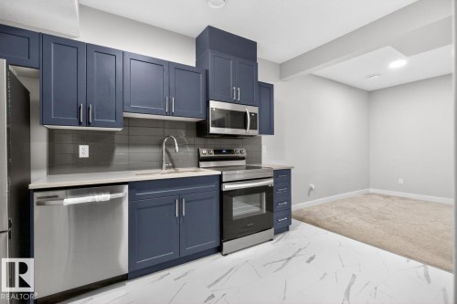 Kitchen featuring blue shaker-style cabinetry, stainless steel appliances, light-colored countertops, and a gray subway tile backsplash - 3214 9 Street, Edmonton, AB - Indoor Photo Showing Kitchen With Stainless Steel Kitchen