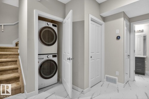 Dedicated laundry area featuring a stacked washer and dryer, adjacent to a carpeted staircase with a wood handrail - 3214 9 Street, Edmonton, AB - Indoor Photo Showing Laundry Room