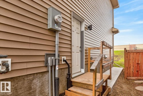 Exterior featuring tan vinyl siding, a white entry door, and a natural wood staircase with handrails - 3214 9 Street, Edmonton, AB - Outdoor With Exterior