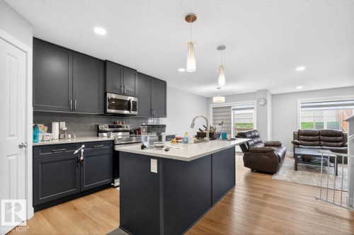 Open-concept kitchen featuring dark cabinetry, stainless steel appliances, a center island with sink, light countertops, and wood-finish flooring - 3214 9 Street, Edmonton, AB - Indoor Photo Showing Kitchen With Upgraded Kitchen