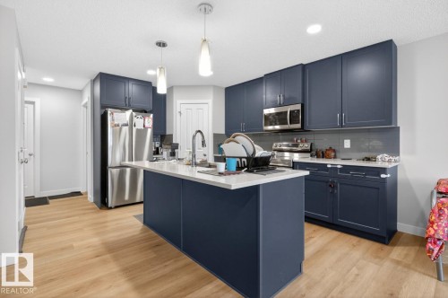 Kitchen featuring an expansive island, dark blue cabinetry, wood-finish flooring, stainless steel appliances, and recessed lighting - 3214 9 Street, Edmonton, AB - Indoor Photo Showing Kitchen With Stainless Steel Kitchen With Upgraded Kitchen