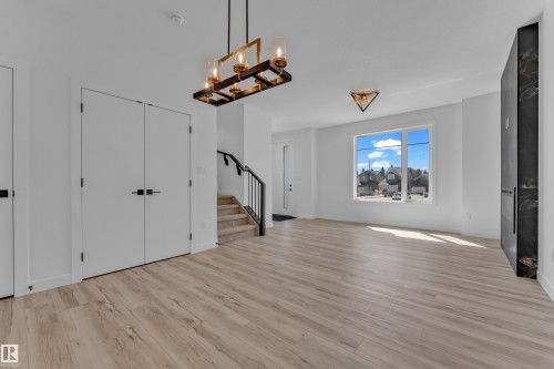 Spacious room featuring wood-finish flooring, a contemporary chandelier, a built-in dark stone fireplace, and abundant natural light from a large window - 171 Graybriar Drive, Stony Plain, AB - Indoor Photo Showing Other Room