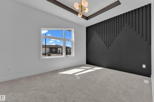 Vaulted ceiling room featuring a decorative tray ceiling with a contemporary chandelier, a window with white trim, and a striking accent wall with a geometric slat design - 171 Graybriar Drive, Stony Plain, AB - Indoor Photo Showing Other Room