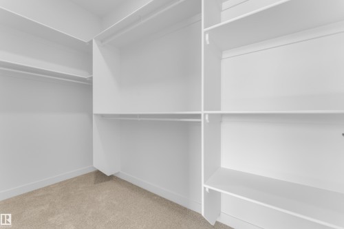 Spacious walk-in closet featuring white built-in shelving, multiple hanging rods, and light beige carpeting - 171 Graybriar Drive, Stony Plain, AB - Indoor With Storage