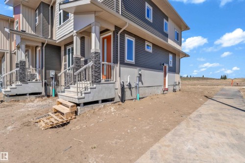 Contemporary townhome exterior featuring multi-toned siding, a bright orange entry door, stone-clad pillars, and white-framed windows - 171 Graybriar Drive, Stony Plain, AB - Outdoor