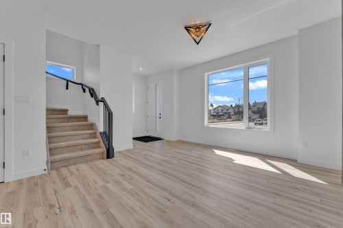 Open-concept living space with light wood-finish flooring, a contemporary staircase featuring a dark railing, and a prominent picture window - 171 Graybriar Drive, Stony Plain, AB - Indoor Photo Showing Other Room
