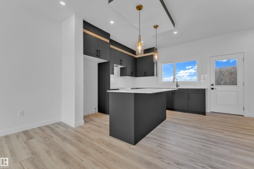 Modern kitchen featuring dark cabinetry, a central island with a light countertop, white subway tile backsplash, and light wood-finish flooring - 171 Graybriar Drive, Stony Plain, AB - Indoor Photo Showing Kitchen