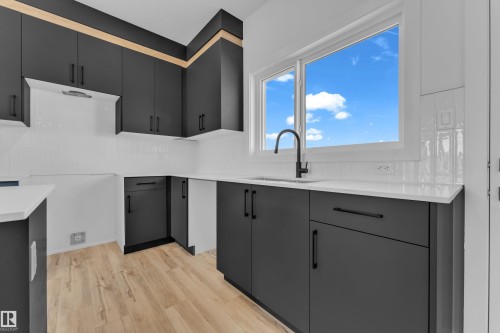 Modern kitchen featuring dark cabinetry with contrasting light wood accents, white countertops, a large window, a matte black gooseneck faucet, and light wood-finish flooring - 171 Graybriar Drive, Stony Plain, AB - Indoor Photo Showing Kitchen