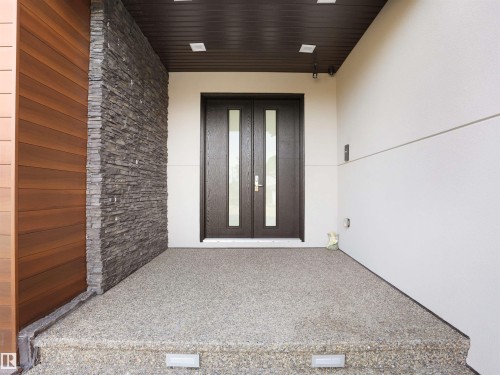 Modern entryway featuring double doors with frosted glass inserts, a stacked stone accent wall, and horizontal wood-finish siding - 913 Wood Place, Edmonton, AB -  With Exterior
