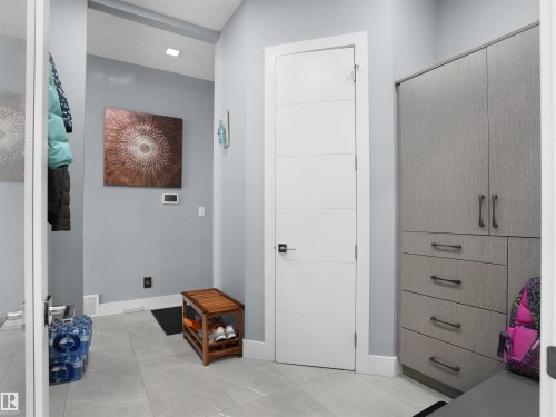 Entryway featuring light gray tile flooring, a modern white paneled door with dark hardware, and a built-in storage unit with textured gray cabinetry and dark pulls - 913 Wood Place, Edmonton, AB - Indoor Photo Showing Other Room