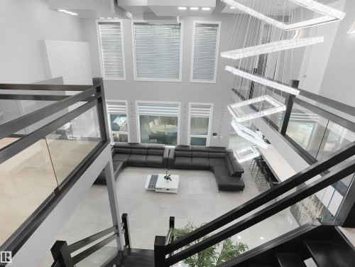Two-story living area featuring a multi-tiered chandelier, extensive window array, light-toned flooring, an open-concept layout, and dark-toned staircase with glass railings - 913 Wood Place, Edmonton, AB - Indoor Photo Showing Other Room