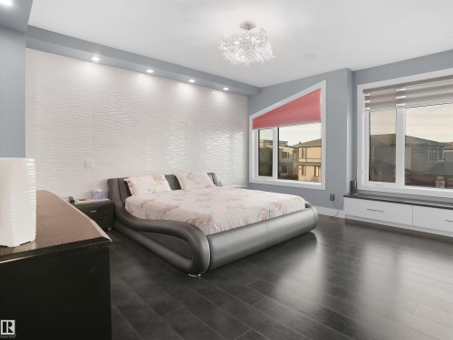 Spacious room featuring dark wood-finish flooring, a textured accent wall with recessed lighting, and a contemporary chandelier - 913 Wood Place, Edmonton, AB - Indoor Photo Showing Bedroom