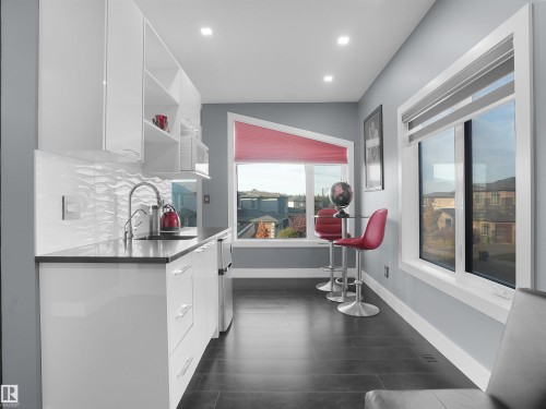 Modern kitchenette featuring white flat-panel cabinetry, a stainless steel sink with a gooseneck faucet, a textured white tile backsplash, and dark countertop - 913 Wood Place, Edmonton, AB - Indoor