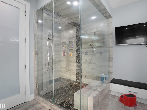 Glass-enclosed shower with pebble-tile flooring and a built-in bench - 913 Wood Place, Edmonton, AB - Indoor Photo Showing Bathroom