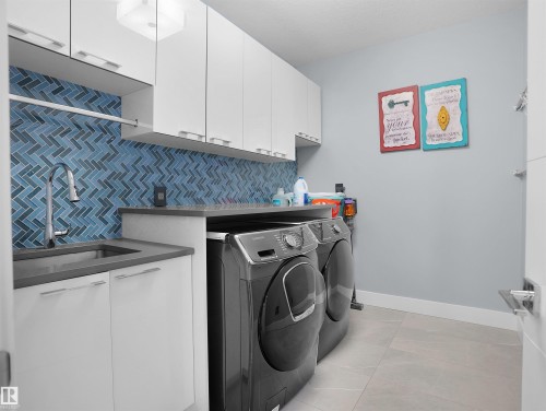 Laundry area featuring a herringbone-patterned blue tile backsplash, stainless steel sink, and light gray countertops - 913 Wood Place, Edmonton, AB - Indoor Photo Showing Laundry Room