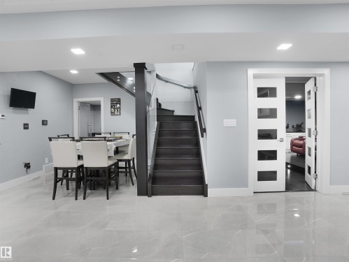 Contemporary interior featuring large format tile flooring, recessed lighting, a modern staircase with dark wood treads and glass railing, and a dining area with a built-in television mount - 913 Wood Place, Edmonton, AB - Indoor Photo Showing Other Room