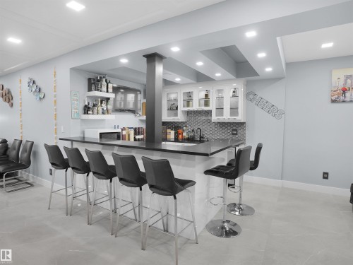 Built-in bar featuring a dark countertop, white cabinetry with glass inserts, and a honeycomb tile backsplash - 913 Wood Place, Edmonton, AB - Indoor