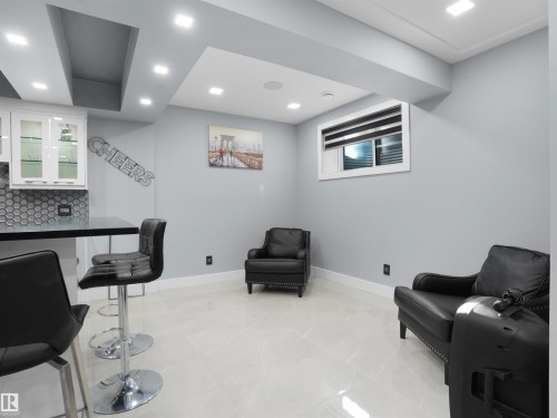 Finished basement area featuring recessed lighting, a wet bar with white cabinetry, a hexagonal tile backsplash, a dark countertop, and light-toned tile flooring - 913 Wood Place, Edmonton, AB - Indoor