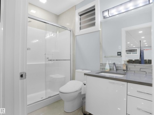 Bathroom featuring a glass-enclosed shower, a modern vanity with a dark countertop and integrated sink, a rectangular mirror, and a wall-mounted light fixture - 913 Wood Place, Edmonton, AB - Indoor Photo Showing Bathroom