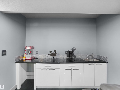 Wet bar featuring a dark countertop, stainless steel sink, modern white cabinetry with chrome hardware, and a gray subway tile backsplash - 913 Wood Place, Edmonton, AB - Indoor Photo Showing Other Room