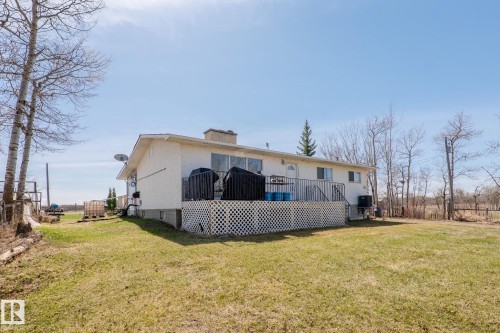 Rear exterior featuring a white stucco finish, an upper-level deck with white lattice skirting, and a visible chimney - 23133 Twp Rd 502, Rural Leduc County, AB - Outdoor