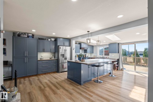 Spacious kitchen featuring wood-finish flooring, blue cabinetry, a central island with seating, a stainless steel refrigerator, and recessed lighting - 23133 Twp Rd 502, Rural Leduc County, AB - Indoor Photo Showing Kitchen With Upgraded Kitchen