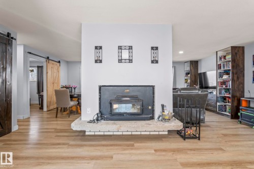 Central fireplace with a stone hearth, wood-finish flooring, two natural wood barn doors, and built-in shelving units - 23133 Twp Rd 502, Rural Leduc County, AB - Indoor Photo Showing Living Room With Fireplace