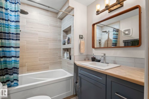 Bathroom featuring a white tub with light-toned tiled surround, built-in shower niches, a vanity with a light wood-finish countertop, and a vessel sink with a chrome faucet - 23133 Twp Rd 502, Rural Leduc County, AB - Indoor Photo Showing Bathroom
