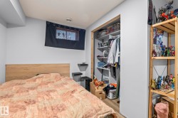 Bedroom featuring light-toned walls, wood-finish headboard, a built-in closet with shelving and hanging space, a small window, and floating wall shelves - 