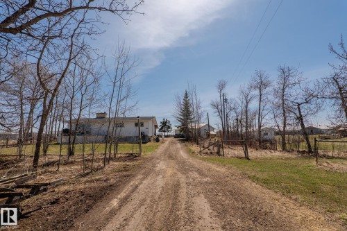 Unpaved driveway leading to a single-story residence with white siding and a prominent chimney - 23133 Twp Rd 502, Rural Leduc County, AB - Outdoor