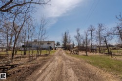 Unpaved driveway leading to a single-story residence with white siding and a prominent chimney - 