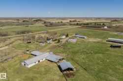 Expansive agricultural property featuring multiple outbuildings, open fields, and wooded areas - 