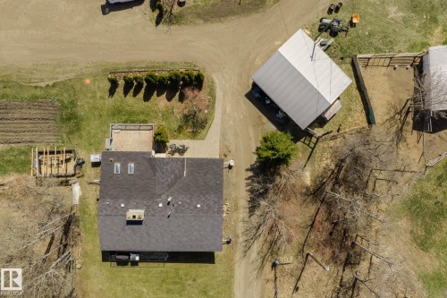 Expansive property featuring a main residence with a dark shingle roof and skylights, a detached outbuilding with a light metal roof, a fenced enclosure, and a cultivated garden area - 23133 Twp Rd 502, Rural Leduc County, AB - Outdoor With View