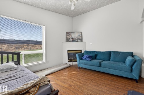 Living area featuring wood-finish flooring, a white fireplace surround with a dark insert, and a large window with horizontal blinds - 4603 126 Avenue, Edmonton, AB - Indoor Photo Showing Other Room