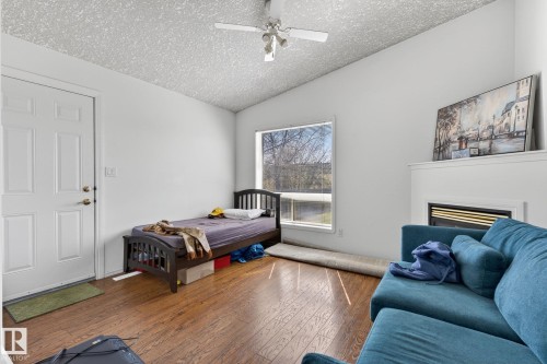 Living area featuring wood-finish flooring, a white paneled entry door, and a built-in fireplace with a white mantel - 4603 126 Avenue, Edmonton, AB - Indoor Photo Showing Bedroom