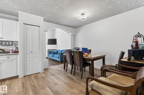 Open-concept living space featuring wood-finish flooring, white cabinetry, a built-in electric fireplace, and an arched entryway - 4603 126 Avenue, Edmonton, AB - Indoor