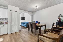 Open-concept living space featuring wood-finish flooring, white cabinetry, a built-in electric fireplace, and an arched entryway - 