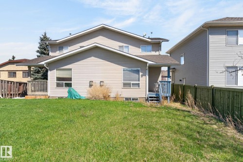 Spacious rear yard with a green lawn, featuring a light-colored vinyl-sided exterior and a wooden deck - 4603 126 Avenue, Edmonton, AB - Outdoor With Exterior