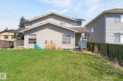 Spacious rear yard with a green lawn, featuring a light-colored vinyl-sided exterior and a wooden deck - 