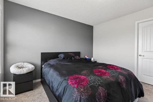 Bedroom featuring a two-tone wall design with a dark accent wall, textured ceiling, light-toned carpet flooring, and a white paneled interior door - 17540 58 Street Nw, Edmonton, AB 