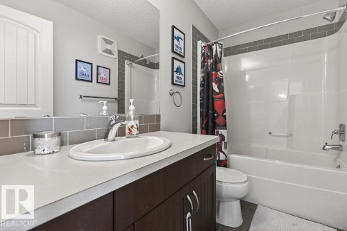 Bathroom featuring a built-in vanity with a composite countertop and integrated sink, a large wall-mounted mirror, and a full-size bathtub with a shower - 17540 58 Street Nw, Edmonton, AB 