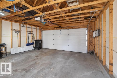 Spacious garage featuring a concrete floor, exposed wood framing, and a white overhead garage door with an automatic opener - 17540 58 Street Nw, Edmonton, AB 