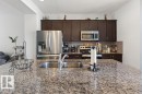Kitchen featuring a granite-finish island with an undermount double basin sink, stainless steel appliances, dark wood-finish cabinetry, and a subway tile backsplash - 17540 58 Street Nw, Edmonton, AB 